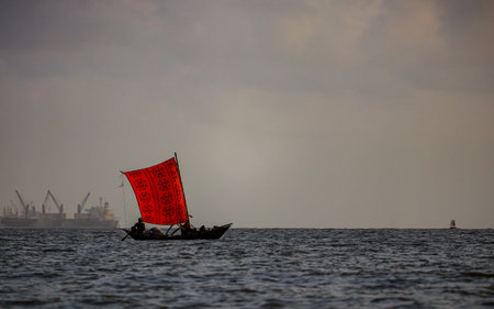 Beautiful landscape of handcrafted wooden boat with a vibrant patterned red sail glides through the Bay of Bengal, reflecting the timeless heritage of coastal life at Bangladesh.の写真素材