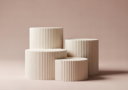 Four fluted, cylindrical podiums of varying heights are arranged on a blush-toned surface, creating a minimalist display for product showcasing. Soft, diffused lighting enhances the subtle textures.の素材