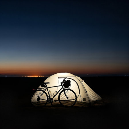 A bicycle is silhouetted inside a glowing tent at dusk, with a distant city skyline visible on the horizon. The scene evokes a sense of adventure and solitude.の素材