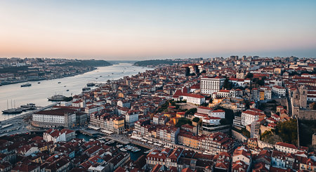 An expansive aerial perspective captures the charming Ribeira district of Porto, Portugal, bathed in the soft glow of dusk, with the Douro River flowing serenely.の素材