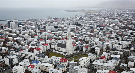 Expansive aerial view of Reykjavik, Iceland, under a soft, grey sky. The striking white Landakotskirkja Cathedral is a focal point among the city's colorful rooftops.の素材