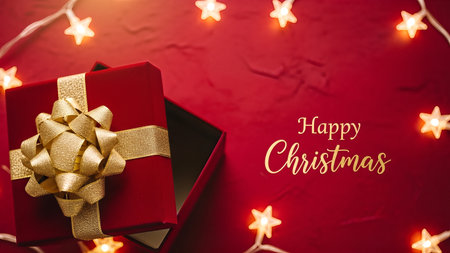 Gift box with golden bow on red background with glowing Christmas lights.の素材