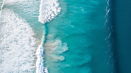 A stunning top-down aerial view captures the ocean's dynamic layers, from lacy white waves crashing to serene turquoise shallows and the vast, deep blue sea.の素材