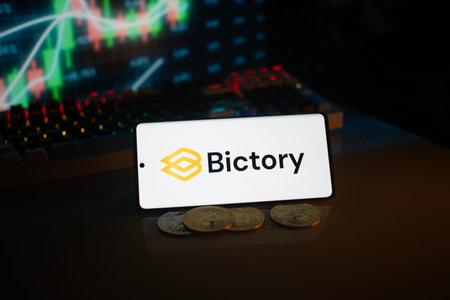 Dhaka, Bangladesh 18 September 2025:Bictory logo on smartphone amidst coins and stock chart,...