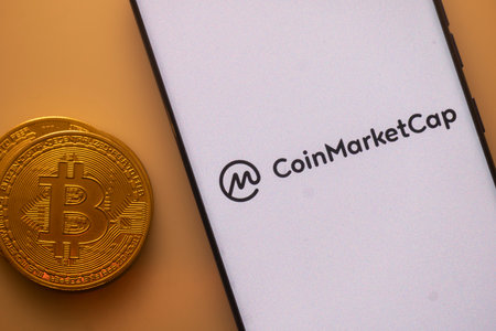 Dhaka, Bangladesh 22 September 2025:Bitcoin coin beside a white phone screen displaying the CoinMarketCap logoのeditorial素材