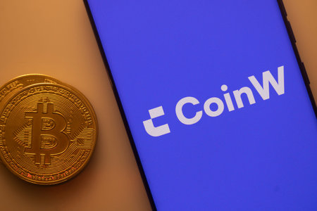 Dhaka, Bangladesh 22 September 2025:Bitcoin coin beside smartphone displaying CoinW app with purple...