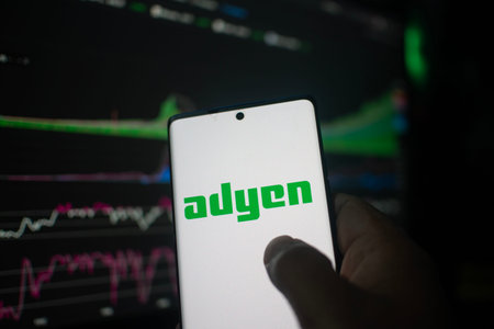 Dhaka, Bangladesh 20 Feb 2026:Hand holding phone displaying Adyen logo against stock chart backdrop