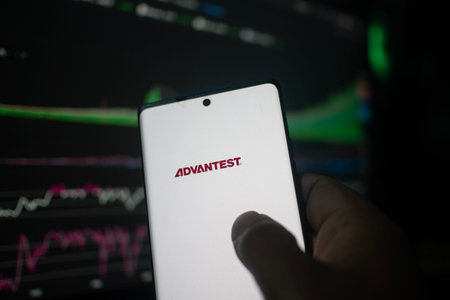 Dhaka, Bangladesh 20 Feb 2026:Hand holding phone displaying Advantest logo against stock chart backdropのeditorial素材