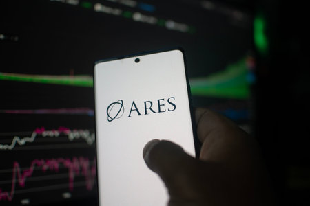 Dhaka, Bangladesh 20 Feb 2026:Hand holding phone displaying Ares logo against stock chart backdrop