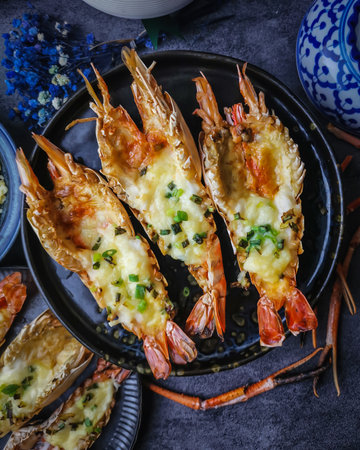 Grilled tiger prawns with cheese and herbs on a black plateの写真素材