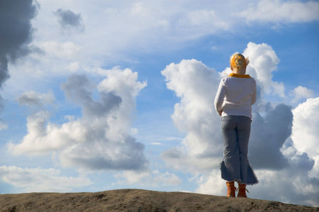 girl on look out on hilltop against sky with big cloudsの写真素材