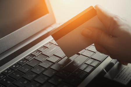 Plastic credit card in hand and a laptop keyboardの写真素材