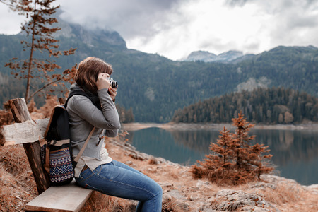Woman with vintage camera sitting on bench at nature landscapeの写真素材