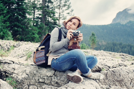 Woman traveler with vintage camera sitting on rocks, nature landscapeの写真素材