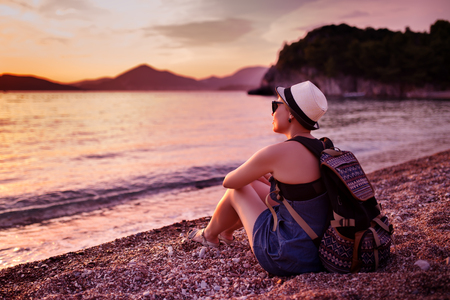 Woman sitting on pebble beach near sea at sunsetの写真素材