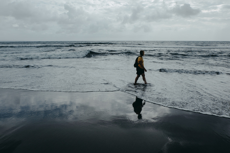 Woman is walking on sea beach. Sky reflected on wet sand. Film color tonedの写真素材