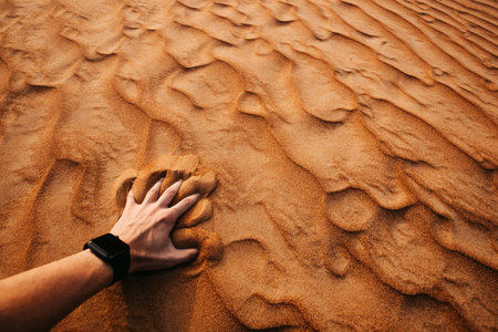 Man hand is touching sand in a desert at sunset