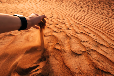 Male hand is pouring dropping sand in a desert at sunsetの写真素材