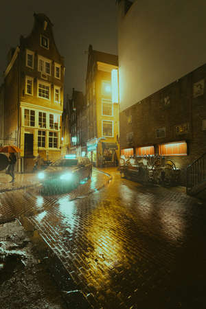 Amsterdam, Netherlands - March 5, 2020: People are walking on the street in Amsterdam city center old town at night in the rainのeditorial素材