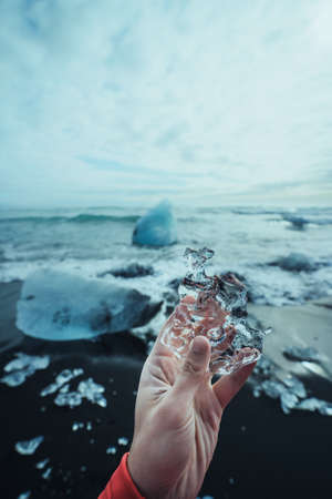 Hand holding ice piece at Diamond Beach (Jokulsarlon - JÃ¶kulsÃ¡rlÃ³n) landscape in East Iceland. Ice on black volcanic sand in the dayの写真素材