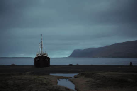 Abandoned ship at West Fjords region in north Iceland. Gardar BA64 is oldest steel ship in Iceland, beached at Patreksfjordur. Dramatic moody sky landscapeの写真素材