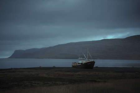 Abandoned ship at West Fjords region in north Iceland. Gardar BA64 is oldest steel ship in Iceland, beached at Patreksfjordur. Dramatic moody sky landscapeの写真素材