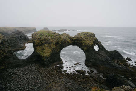 Iceland nature landscape. Gatklettur - Arch Rock, basalt rock cliff in Snaefellsnes peninsula near Arnarstapi village. Stormy waves at rainy weatherの写真素材