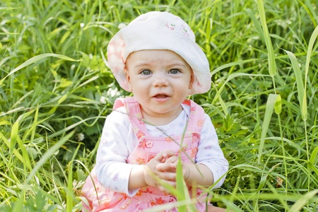 Happy baby girl with blue eyes lying on grassの写真素材