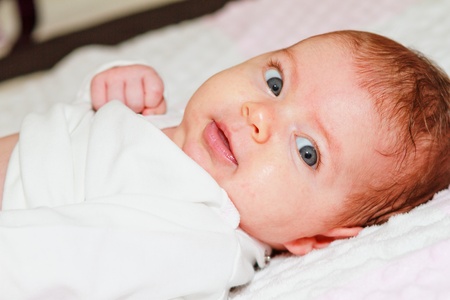 A cute 8 weeks old Caucasian infant smiles as she laying on bed.の写真素材