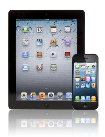 black Apple iPhone 5 in front of a black Apple iPad 3 tablet. Both devices are showing the homepage with the same default wallpaper and are isolated on white on a reflective surface.のeditorial素材
