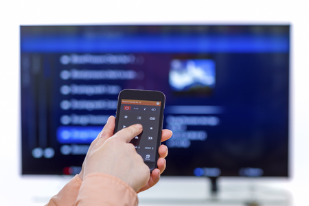 Closeup on woman hand holding smartphone and use a app with remote control  and surfing programs on television. Focus on the remote control.の写真素材