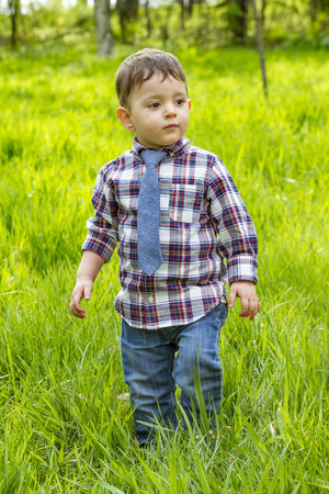 Little boy in shirt and jeans and striped tie walking in the grass in parkの写真素材