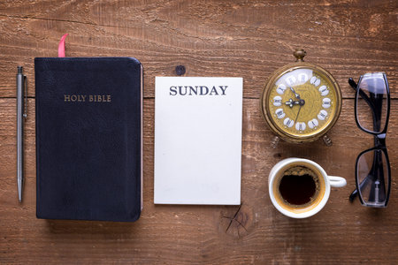 Holy Bible, alarm clock, glasses and coffee on wood table. Studying  the Bible concept.
