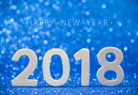 Happy New Year 2018 white wood number on blue paper with glitter lights.