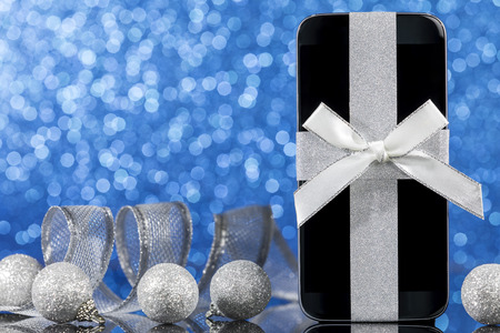 Smartphone and decorations for Christmas tree on black glass table over blue background. Focus on smartphone.の写真素材