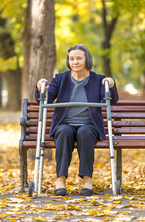 Senior woman with walker getting up from bench and walking outdoors in autumn park. の写真素材