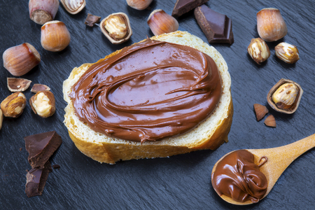 Slice of bread with spread chocolate cream and hazelnuts on black table. Serving a delicious breakfast concept.の写真素材
