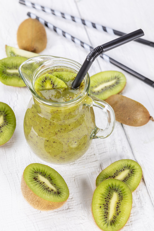 Healthy fresh kiwi smoothie in glass on a wooden background. Focus on kiwi slice in a carafe.の写真素材