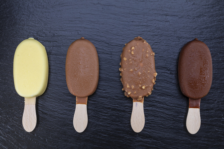 Ice cream on stick covered with chocolate on black stone slate board.の写真素材