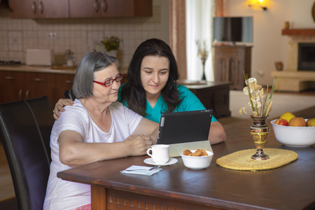 Female nurse and senior woman using tablet PC in kitchen at nursing home.の写真素材