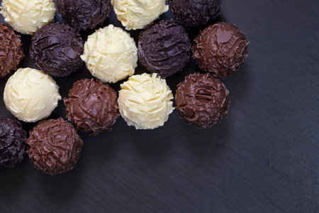 Delicious chocolate truffles on black stone background. Assortment of fine chocolates in white dark...