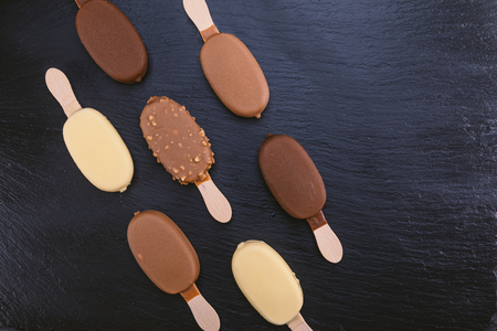 Ice cream on stick covered with chocolate on black stone slate board.の写真素材