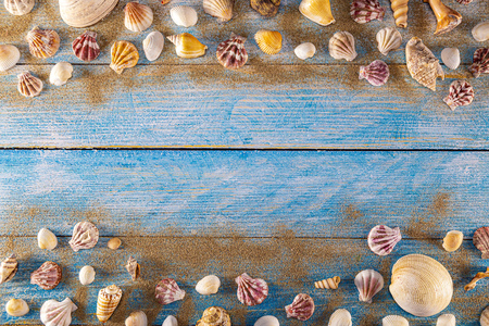 Summer time concept with sea shells on a blue wooden background and sand. Seashells frame on wooden background nautical border. Focus on seashells.