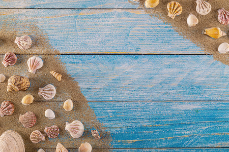 Summer time concept with sea shells on a blue wooden background and sand. Seashells frame on wooden background nautical border. Focus on seashells.の写真素材