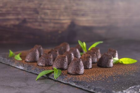Homemade chocolate truffles with mint sprinkled with cocoa powder on slate. Focus on first truffle.の写真素材