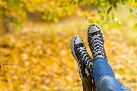 Relaxed teenage girl wearing sneakers is lying on bench in autumn park closeup. Focus on sneakers.の写真素材