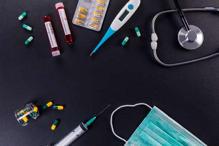 Blood test tube with the Coronavirus disease for virus test and research. Blood test tube with protective masks, medicines, thermometer, stethoscope and syringe on a black background.の写真素材