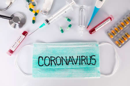 Protective medical mask with Coronavirus text and medical ampoules stethoscope thermometer and pills. Virus test and research for treatment concept.の写真素材