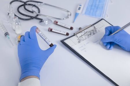 Analyst hands with protective gloves holding COVID 19 Coronavirus test blood making statistical notes. Virus test and research concept. Closeupの写真素材