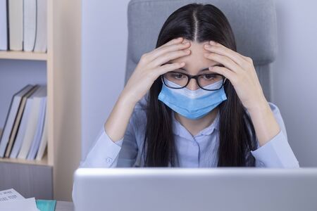 Exhausted businesswoman with mask on her face working in the office during the coronavirus pandemic. Working at home during the pandemic concept.の写真素材